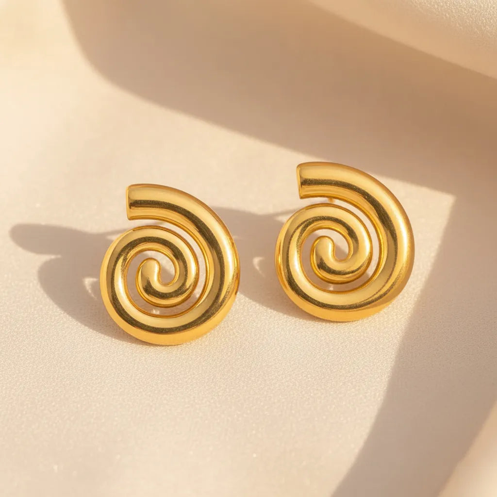 Pair of bold, anti-tarnish gold spiral stud earrings on a cream-colored surface.