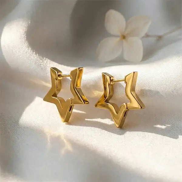 Gold star hoop earrings displayed on white satin fabric with soft sunlight and dried flower