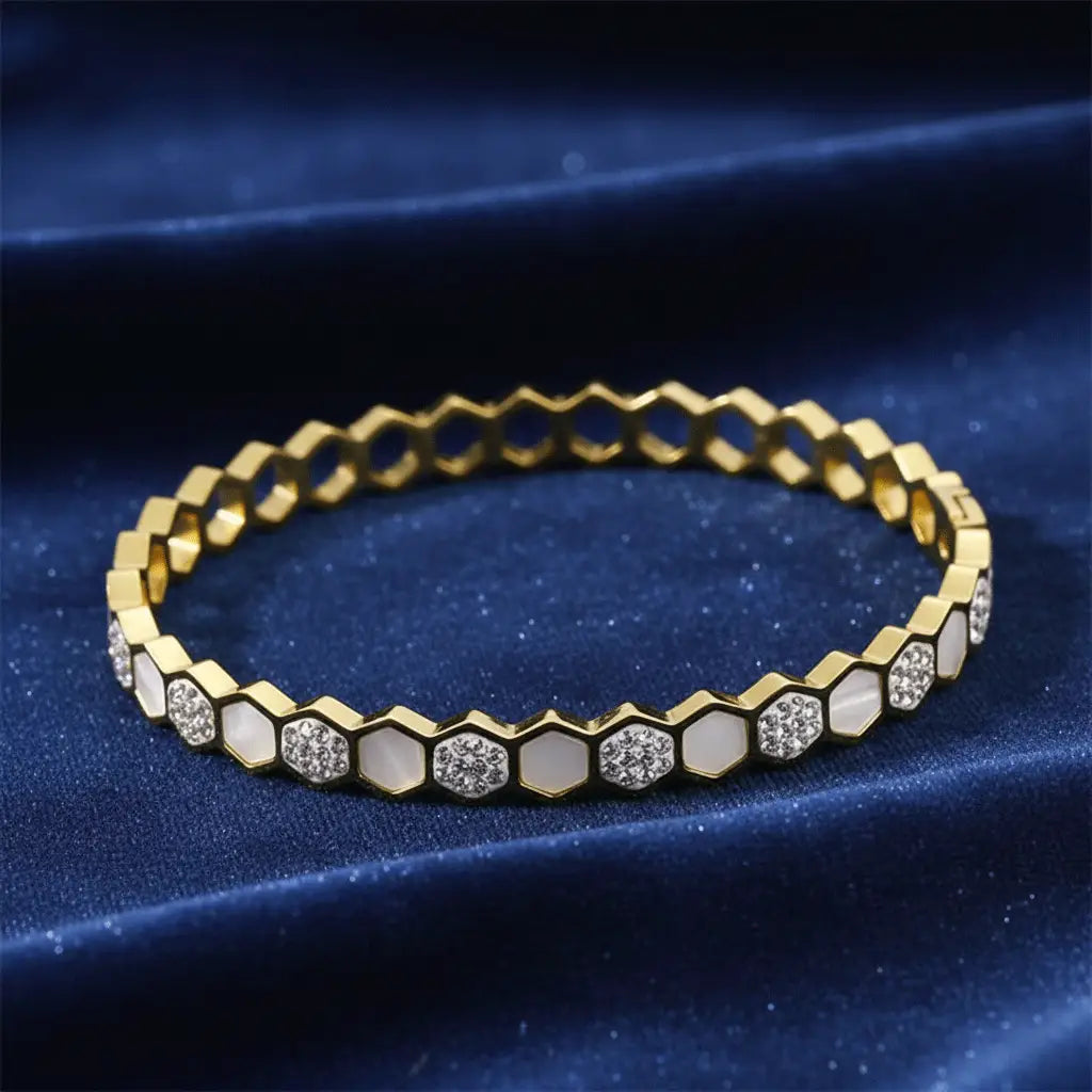 Gold hexa charm bracelet featuring alternating white enamel and diamond-studded segments displayed on dark blue velvet