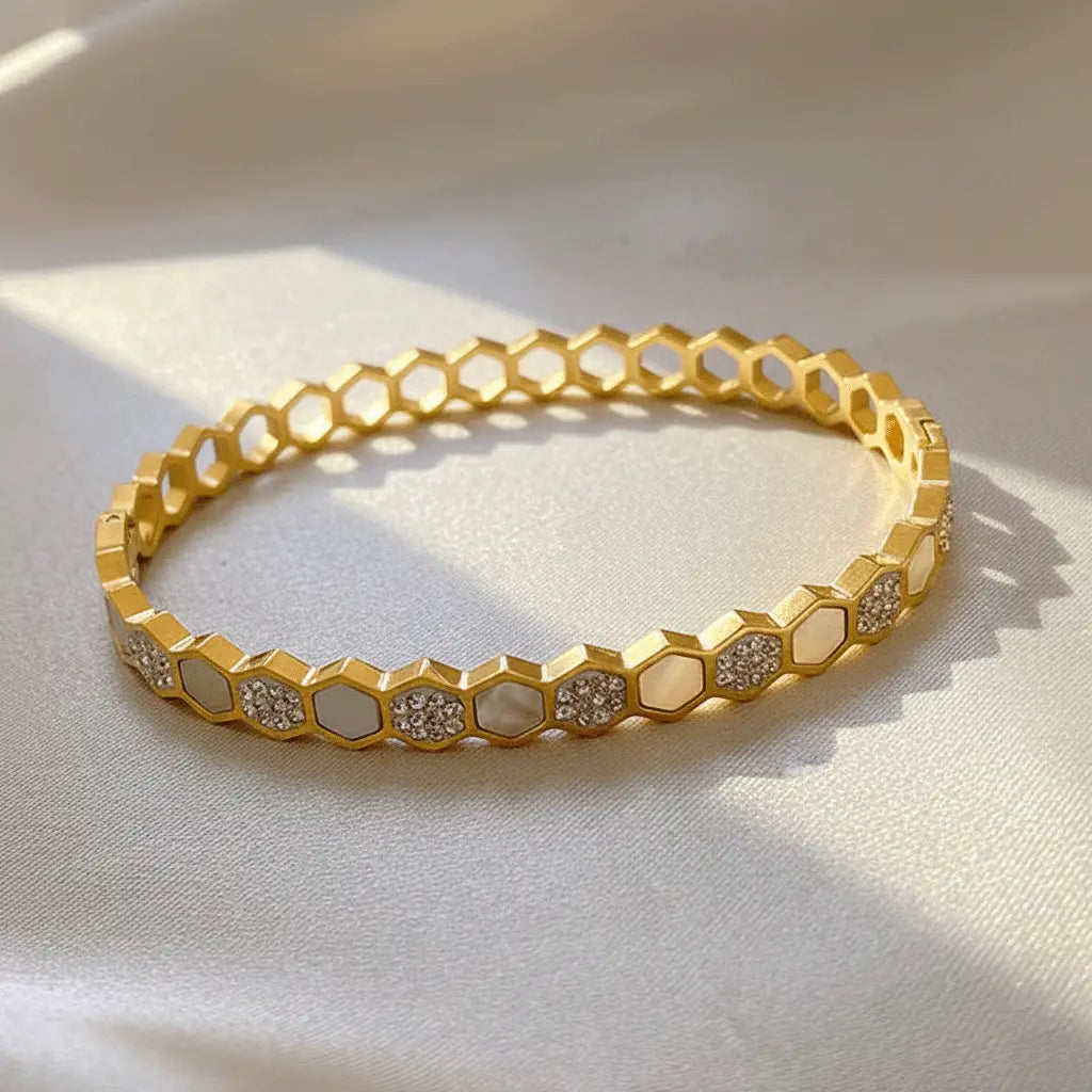 Gold hexa charm bracelet featuring alternating white enamel and diamond-studded segments displayed on beige satin cloth.