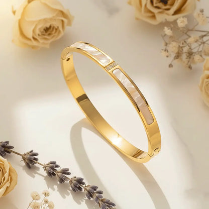 Mother-of-Pearl Gold bracelet featuring elongated mother-of-pearl inlays and a small cluster of crystals, displayed on a softly lit surface with dried roses and lavender sprigs surrounding it.