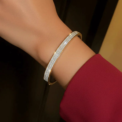 A gold bangle bracelet with two rows of small sparkling stones on wrist.