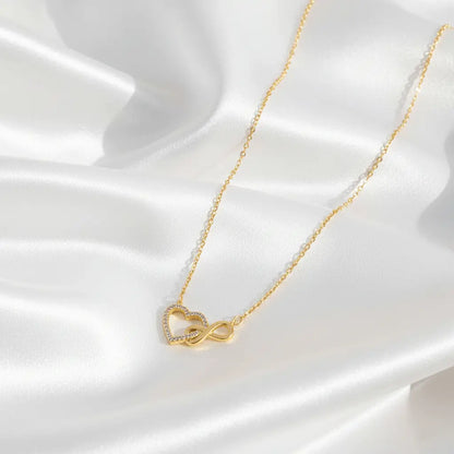 A delicate necklace with a heart-shaped pendant intertwined with an infinity symbol, accented with small crystals, displayed on smooth white satin fabric.