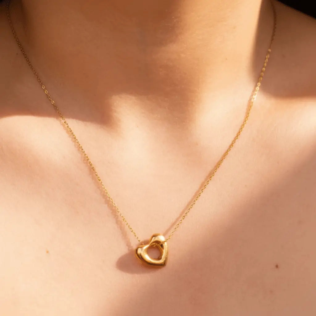 A polished gold heart-shaped pendant with a hollow center hanging from a delicate gold chain