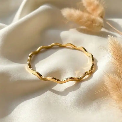 Minimal gold wave bangle anti tarnish jewellery photographed on white fabric with soft sunlight