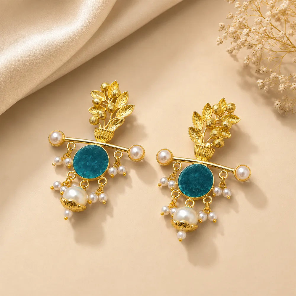 Pair of Aqua Blossom anti tarnish brass earrings with teal blue stones, floral gold finish, and pearl drop detailing on a beige background.