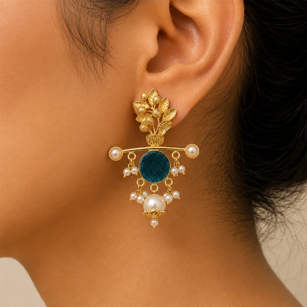 Close-up of Aqua Blossom anti tarnish brass statement earring with teal blue stone, floral brass motif, and pearl embellishments worn by an Indian model.