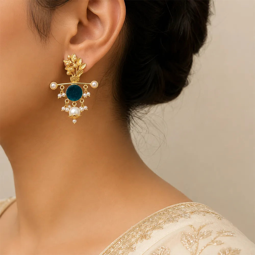 Indian model wearing Aqua Blossom anti tarnish brass earrings featuring a teal blue stone, floral gold-toned design, and pearl danglers.