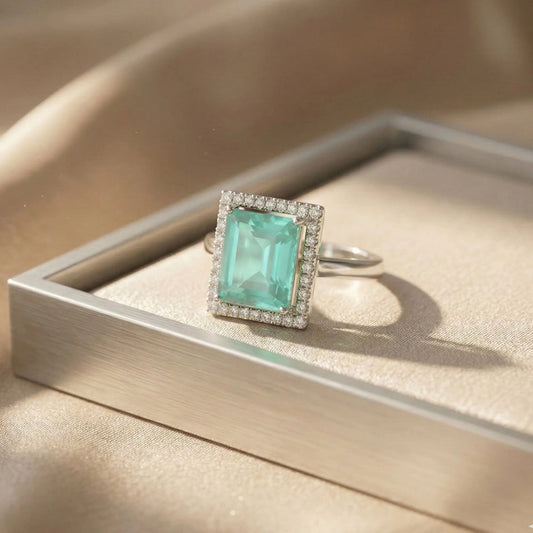 Elegant aqua royale adjustable ring with sparkling AD halo stones displayed on a beige satin jewellery tray in soft natural sunlight.