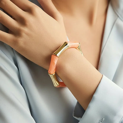 Peach resin and gold bamboo-style bracelet on women's hand.
