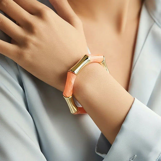 Peach resin and gold bamboo-style bracelet on women's hand.