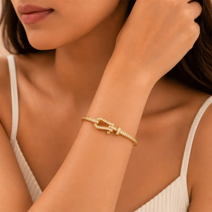 A close-up lifestyle shot of a woman wearing a Belt Buckle Kada. The bracelet features a small central knot or bow design embellished with tiny clear stones, set against a warm, neutral background.