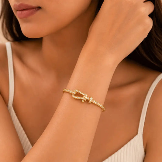 A close-up lifestyle shot of a woman wearing a Belt Buckle Kada. The bracelet features a small central knot or bow design embellished with tiny clear stones, set against a warm, neutral background.