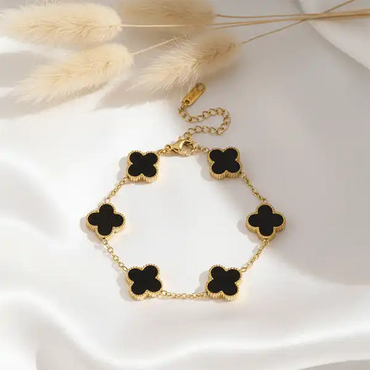 Black Clover Bracelet arranged on white satin cloth with pampas grass, gold bracelet with black clover charms