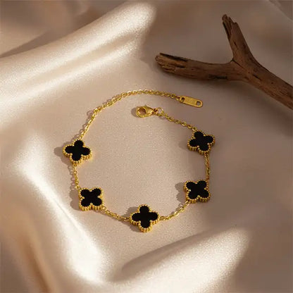Black Clover Bracelet displayed on beige satin cloth with dark wooden branch, gold chain bracelet with black clover charms