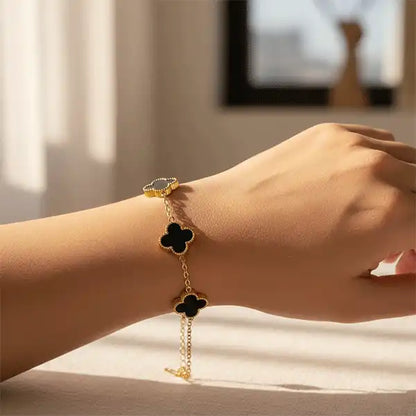 Black Clover Bracelet worn on wrist, gold chain bracelet with black clover enamel charms in natural sunlight