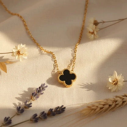Reversible anti-tarnish clover pendant with white and black sides, resting on gold chain, styled with dried flowers.