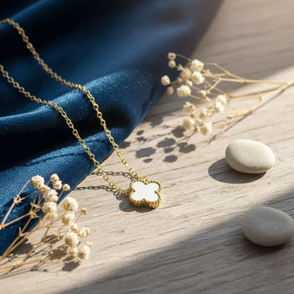 Gold necklace featuring a two-sided anti-tarnish clover pendant, white on one side and black on the other, surrounded by botanicals.