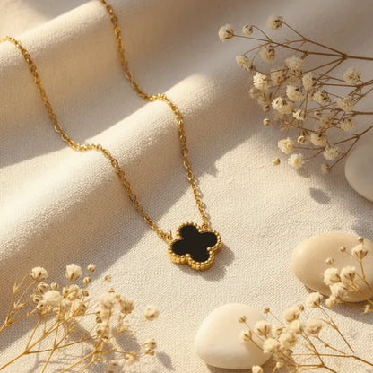 Anti-tarnish gold clover pendant necklace, reversible with white and black, arranged on neutral fabric with floral accents.