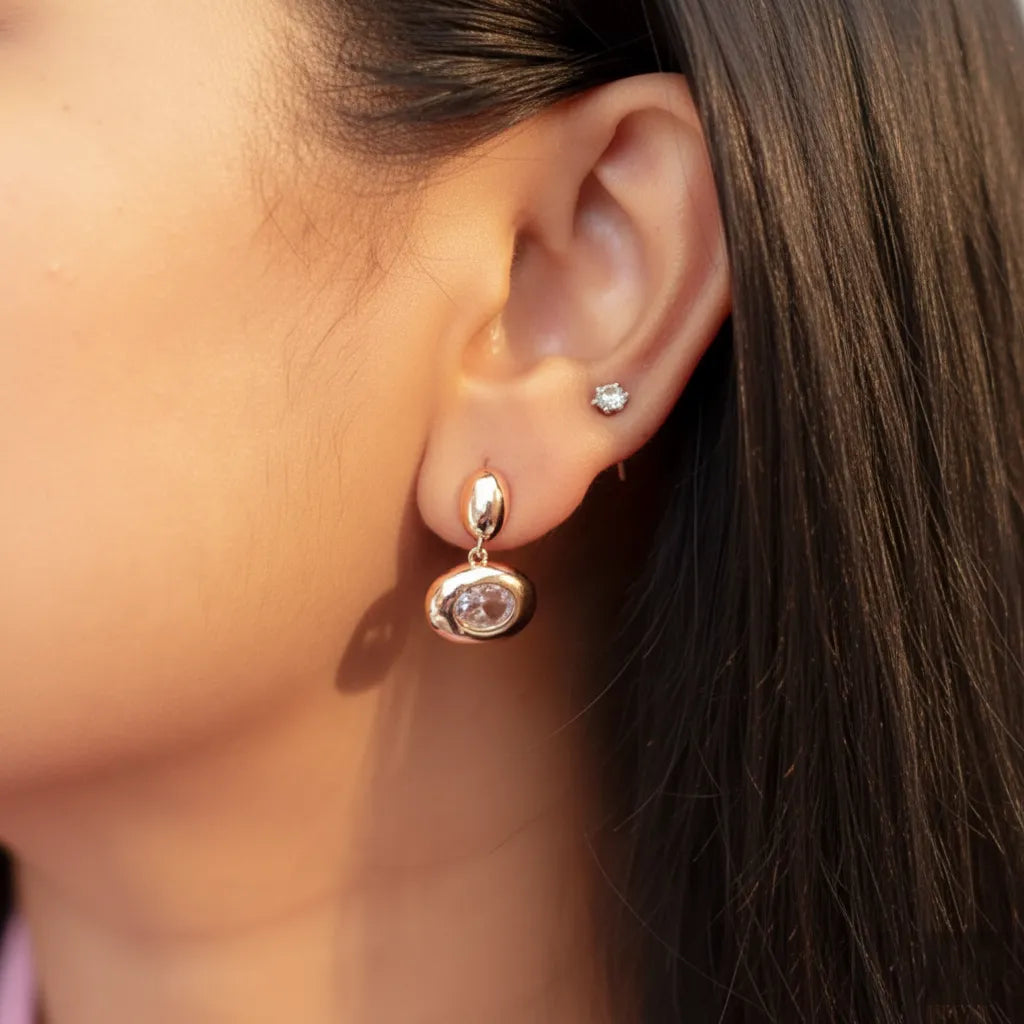 Model wearing Blush Glow Earrings, showcasing rose-gold shine and oval stone detail.