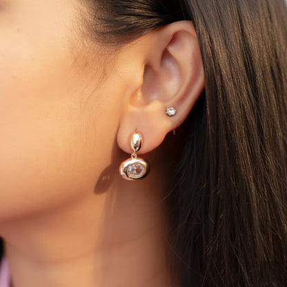 Model wearing Blush Glow Earrings, showcasing rose-gold shine and oval stone detail.