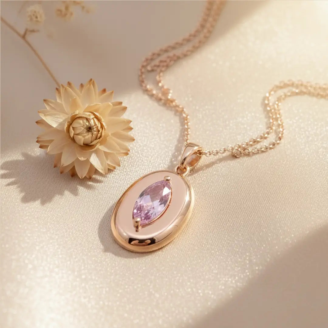 Rose gold necklace with a marquise-cut pink gemstone pendant placed on soft satin fabric beside a dried flower.