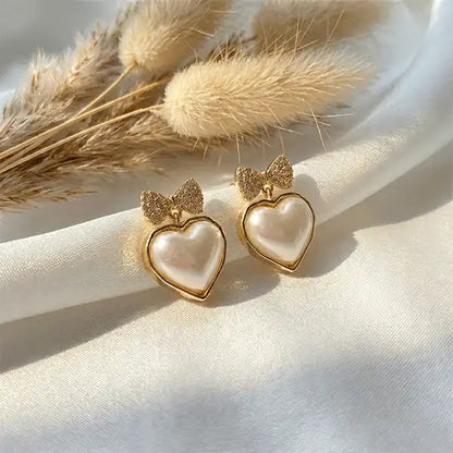 Bow heart pearl drop earrings in gold finish on white satin cloth with pampas grass, anti-tarnish jewellery for women