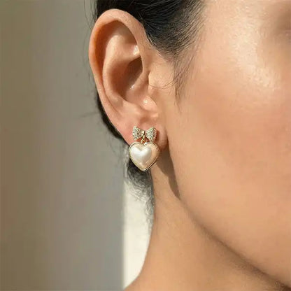 Model wearing bow heart pearl drop earrings in gold finish, anti-tarnish stud earrings close-up ear shot