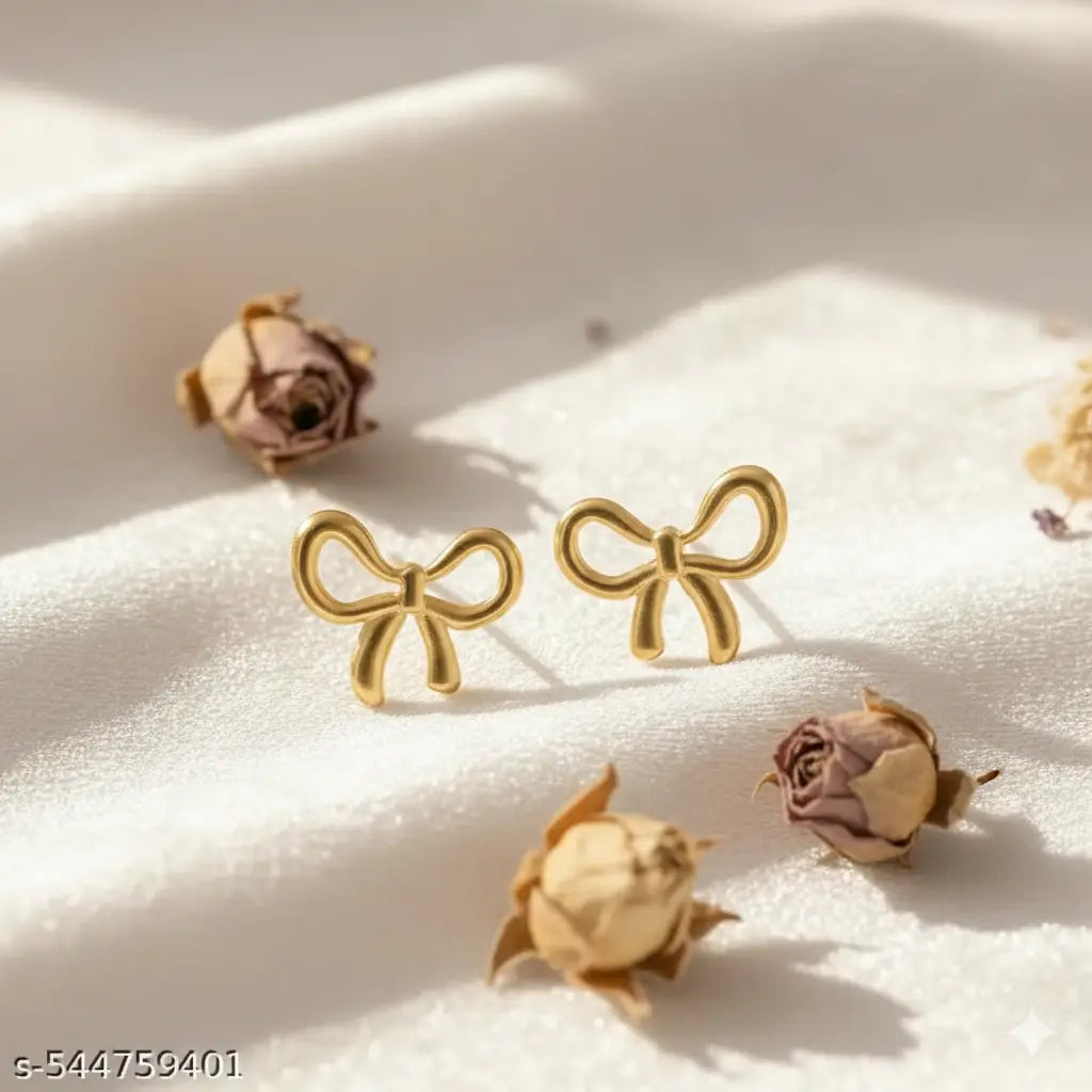 Minimalist gold bow-knot stud earrings displayed on white textured fabric with dried rose buds.