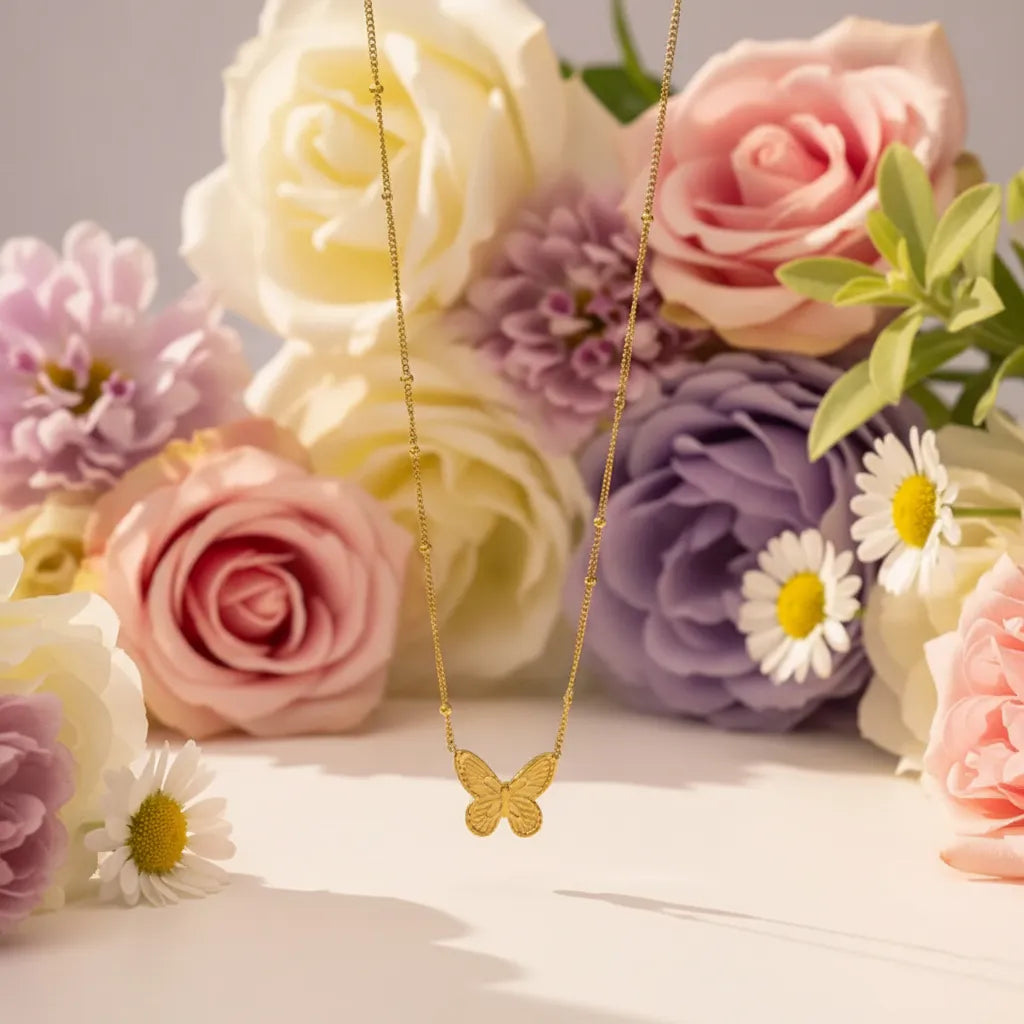 Delicate gold butterfly pendant necklace on a beaded chain with dried flowers in the background.