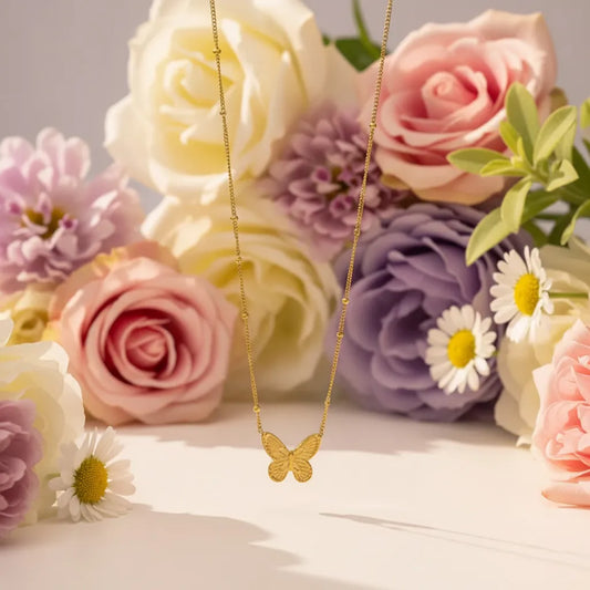 Delicate gold butterfly pendant necklace on a beaded chain with dried flowers in the background.