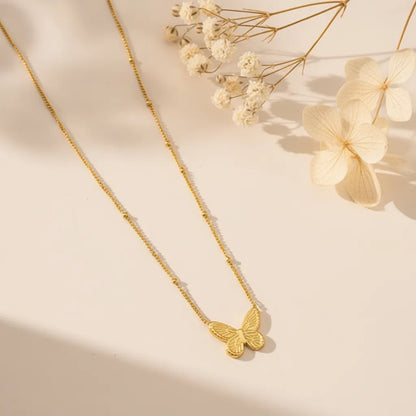 Delicate gold butterfly pendant necklace on a beaded chain with dried flowers in the background.