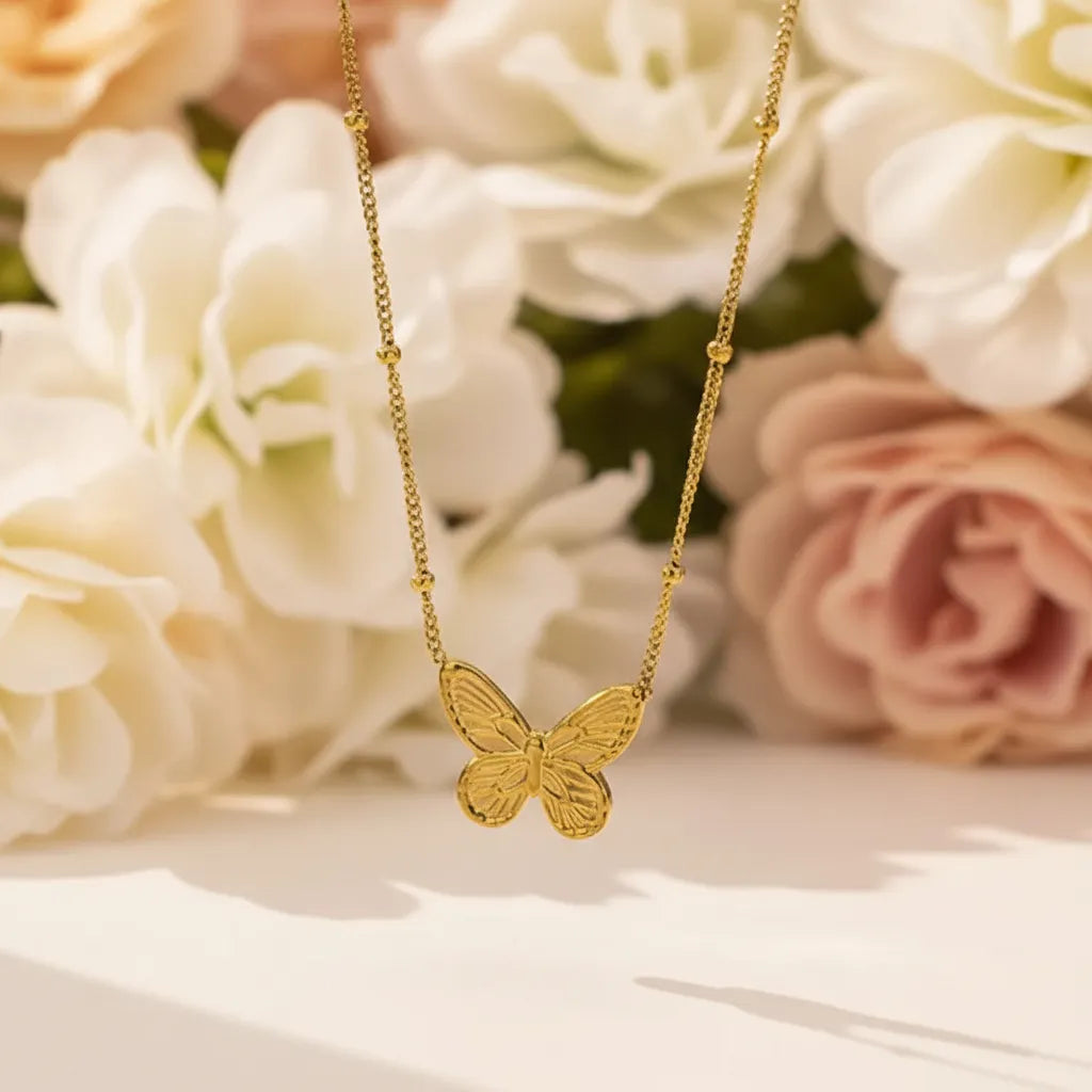Delicate gold butterfly pendant necklace on a beaded chain with dried flowers in the background.