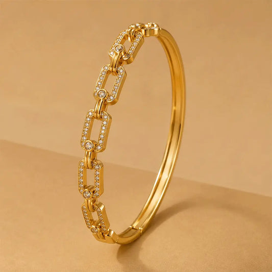 A polished Chain Link Kada with rectangular chain-link motifs, each set with small clear stones, photographed on a warm beige background.