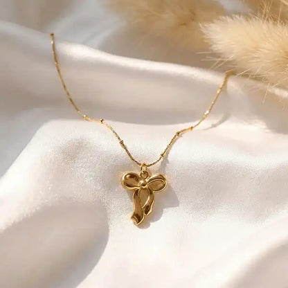Classic bow drop pendant necklace in gold tone placed on white satin fabric with soft sunlight