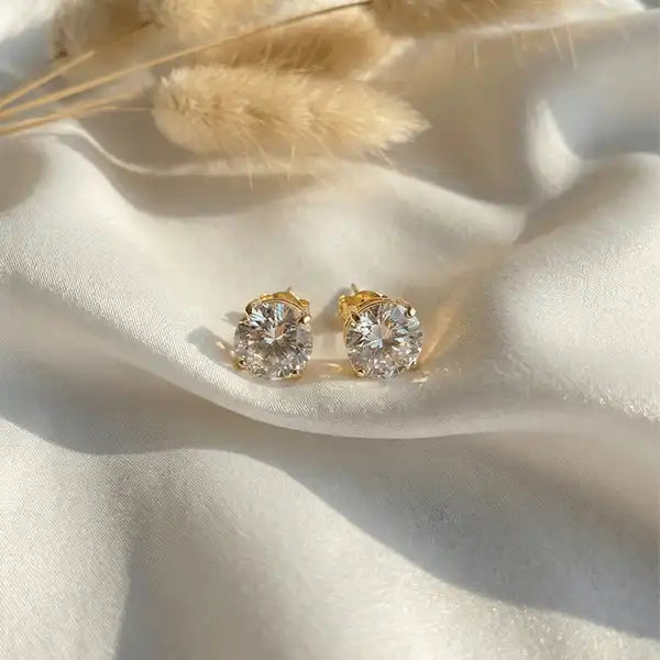 Classic crystal stud earrings in gold setting displayed on white satin background with soft light