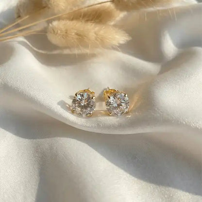 Classic crystal stud earrings in gold setting displayed on white satin background with soft light