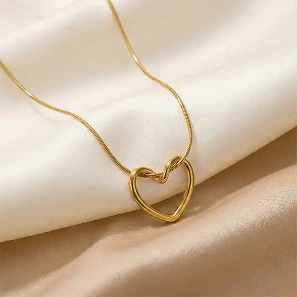 Minimal gold heart pendant necklace placed on beige satin cloth, elegant anti-tarnish jewellery close-up