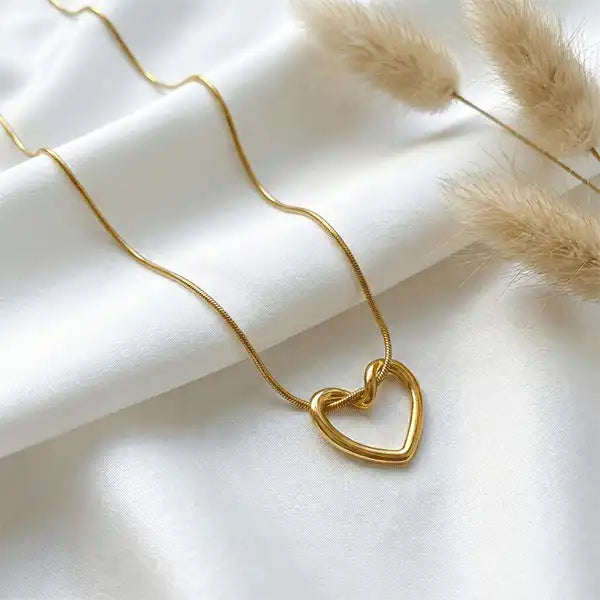 Gold heart pendant necklace on white satin cloth with pampas grass, minimalist anti-tarnish jewellery design