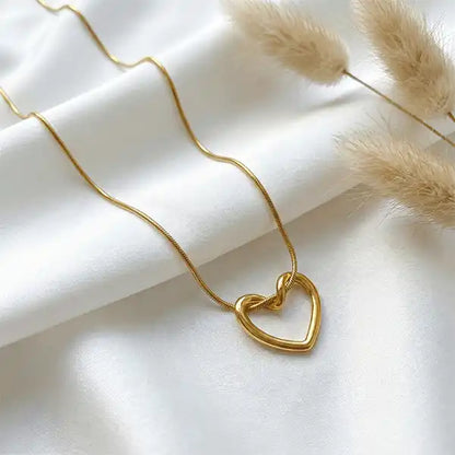 Gold heart pendant necklace on white satin cloth with pampas grass, minimalist anti-tarnish jewellery design
