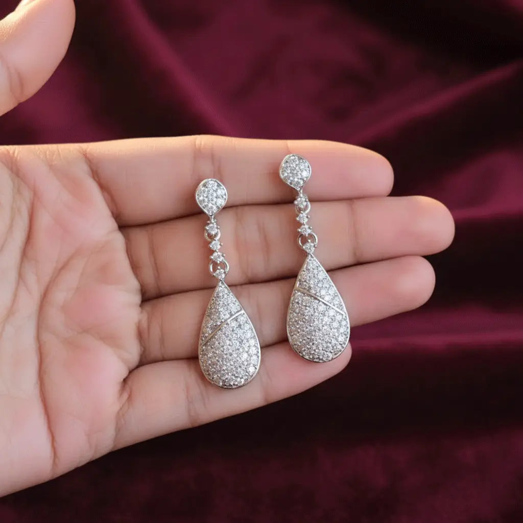 Close-up of silver teardrop AD earrings resting on a hand, showcasing the detailed stone work.
