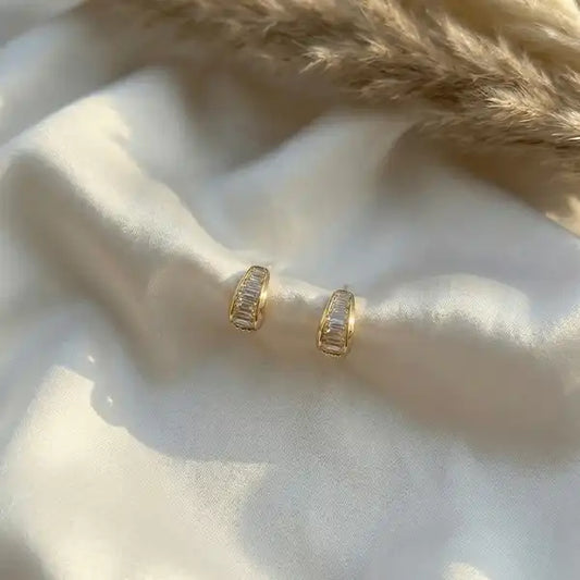 Crystal Curve anti-tarnish gold studs placed on white satin fabric with soft natural sunlight