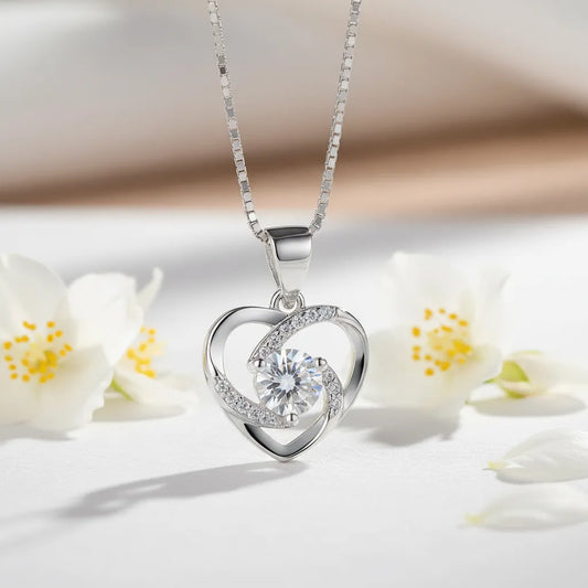 Crystal Heart AD Pendant necklace, a silver heart-shaped design with a brilliant central stone, styled on wood with flowers.