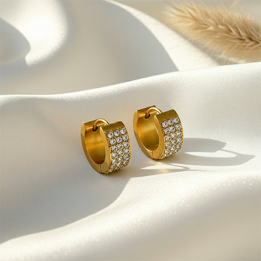 Anti-tarnish gold huggie hoops with crystal detailing displayed on satin background