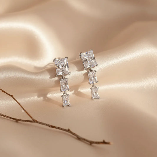 Crystal Square Drops earrings placed on a soft champagne satin fabric, featuring three dangling rectangular crystals.