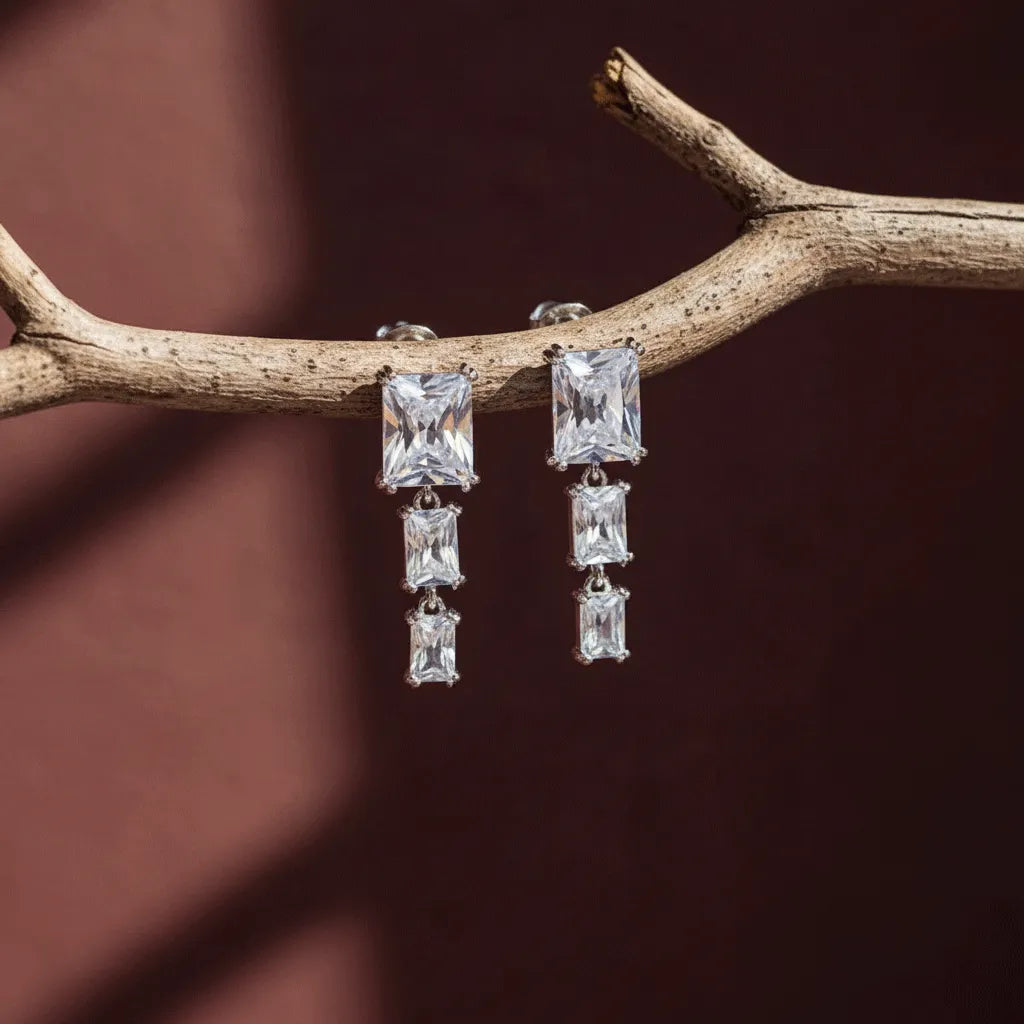 Crystal Square Drops earrings hanging on a textured wooden branch with a warm brown backdrop.