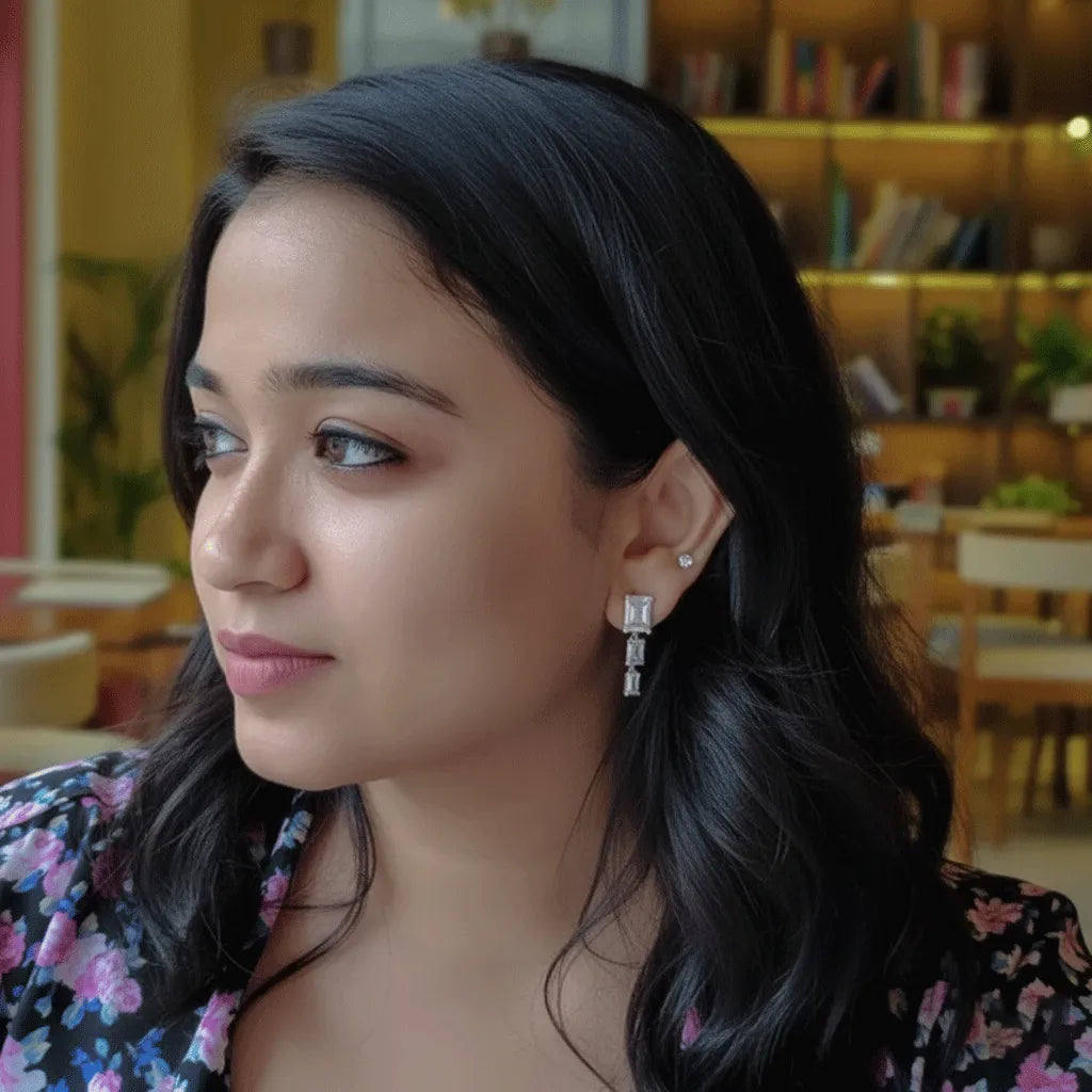 Woman wearing Crystal Square Drops earrings, showcasing dangling rectangular crystals in a natural indoor setting.
