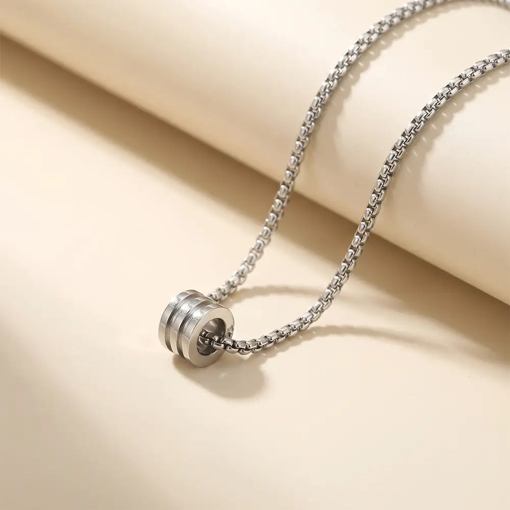 Minimalist silver anti-tarnish cylinder pendant necklace for men displayed on elegant beige studio background from K-A Trends