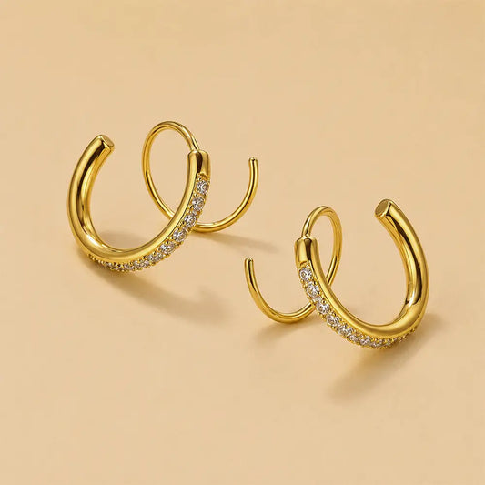 A pair of Dazzle Loop Earrings with a row of small clear stones along the front, displayed on a warm beige background.