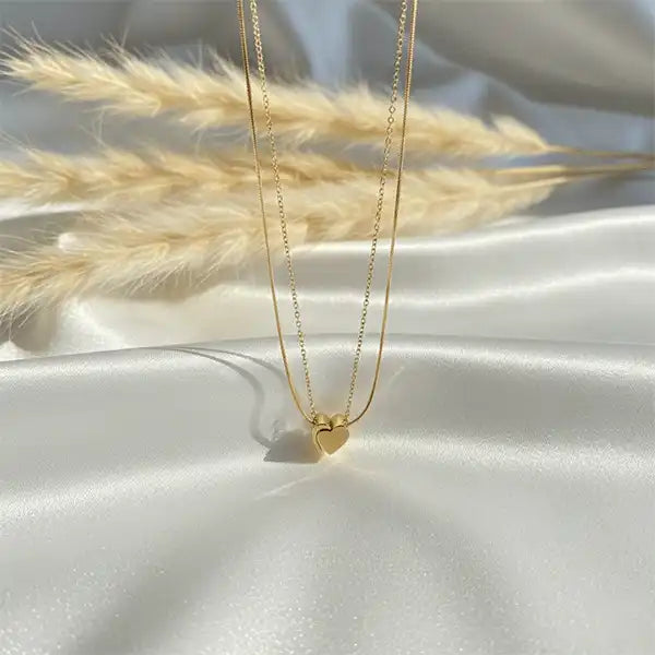 Gold double chain heart pendant necklace displayed on white satin fabric with soft sunlight and pampas grass, anti-tarnish jewellery